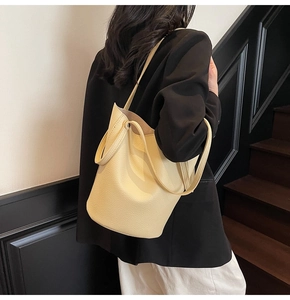 Pale yellow bucket bag in lychee pattern leather shown on shoulder with black blazer