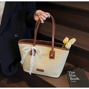 Détail d'un sac cabas en paille tressée avec anses en cuir marron et un nœud en dentelle