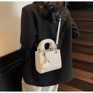 Litchi pattern white handbag with heart charm shown on model in a stylish stairway setting