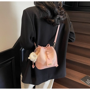 Pink bucket bag with snake texture, drawstring detail, and a white plush ball charm