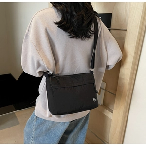 Detail of black nylon crossbody bag with multi-zipper compartments and round logo on model