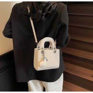 Detail of cream-colored cross-body bag with lychee texture and heart charm on stairs