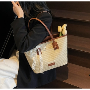 Détail du sac cabas en paille avec poignées en cuir marron et nœud en dentelle blanche