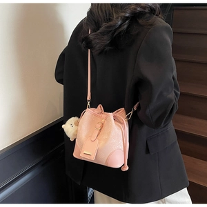 Chic pink bucket bag with snakeskin texture and plush charm worn as a crossbody purse