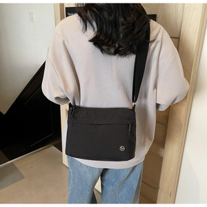 Rear view of model wearing black nylon crossbody tote bag with wide shoulder strap