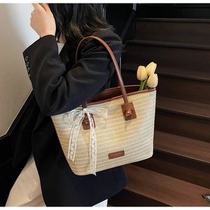 Détail d'un sac cabas en paille tressée avec nœud en dentelle et anses en cuir brun