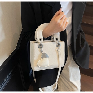 Detail showing white lychee texture leather bag with heart charm and sturdy top handle