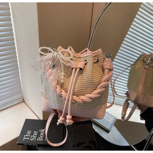 Detail of a woven straw bucket bag with pink leather trim and lace bow accent