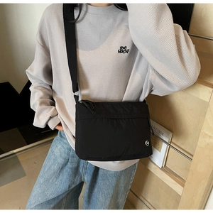 Detail view of black nylon crossbody bag with wide shoulder strap and circular logo