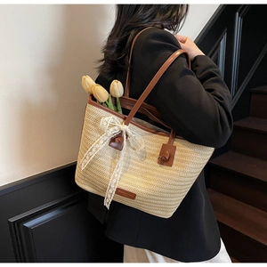 Détail du sac cabas en paille tressée avec nœud en dentelle blanche et anses en cuir brun