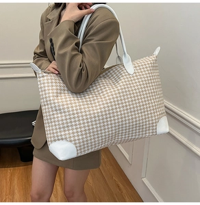 Detail of houndstooth travel bag showing white leather handles and reinforced base corners
