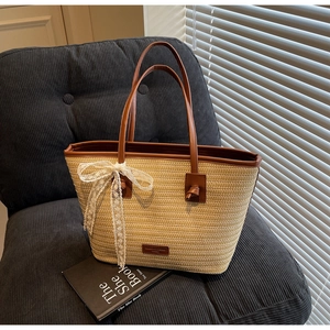 Détail d'un sac cabas en paille tissée beige avec anses en cuir brun et nœud en dentelle