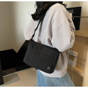 Detail view of black canvas crossbody tote bag with adjustable strap and metal logo accent