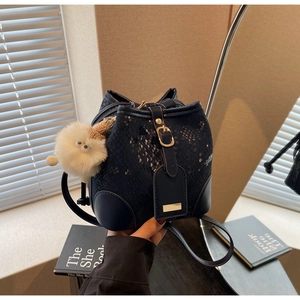 Detail of dark blue faux snakeskin bucket bag with plush charm and gold buckle