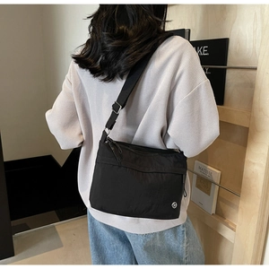 Detailed view of black nylon crossbody bag featuring wide webbing strap and round logo