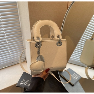 Detail of creamy white pebble leather handbag featuring heart charm and silver hardware