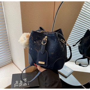 Detail of navy blue snakeskin bucket bag with gold buckle and white plush charm