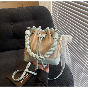 Close-up of woven bucket bag with light blue leather trim, lace bow, and pearl charm