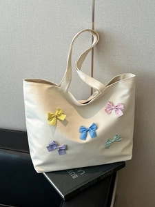 Chic cream checkered tote bag with colorful bows on a book against a gray background
