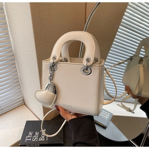 Close-up of white lychee leather handbag with double handles and heart-shaped metal charm