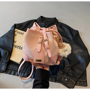 Pink bucket bag with snakeskin texture and cute plush toy charm on black leather background