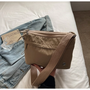 Detail view of khaki multi-zip crossbody bag showing compartments and brand logo