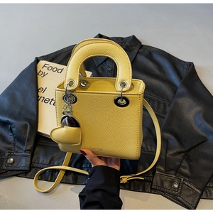 Close-up of yellow lychee leather handbag featuring silver rings and a heart pendant