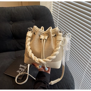 Detail of cream woven bucket bag with pearl chain and lace charms in a lifestyle setting