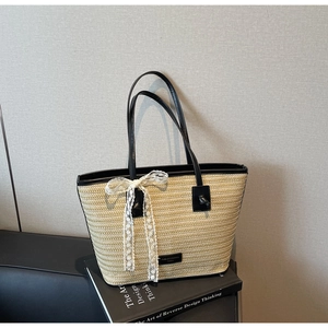Détail d'un grand sac cabas en paille avec poignées noires et un nœud en dentelle blanche