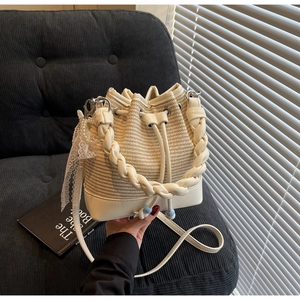 Detail view of woven straw bucket bag with faux leather base and elegant pearl lace charm