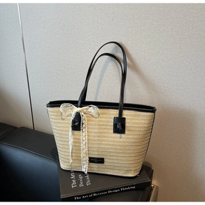 Détail du sac cabas en paille tressée avec poignées en similicuir noir et nœud en dentelle