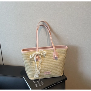 Détail d'un sac cabas en paille avec anses en cuir rose et nœud en dentelle blanche