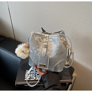 Close-up of silver snakeskin textured bucket bag with gold buckle and plush charm