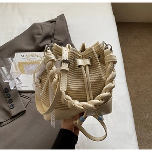 Detail of minimalist woven bucket bag with pearl chain and lace ribbon on soft bedding