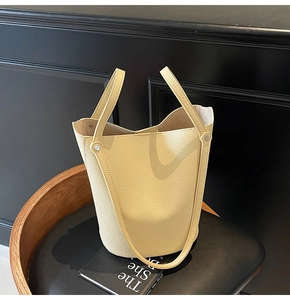 Macro shot of cream-colored bucket bag in litchi grain leather on a leather chair