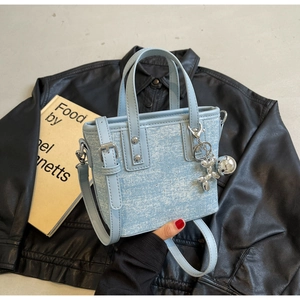 Detail of light blue denim bucket bag with silver balloon dog charm on black leather jacket