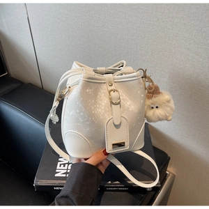 Detail of white bucket bag featuring snake-embossed leather texture and plush monster charm