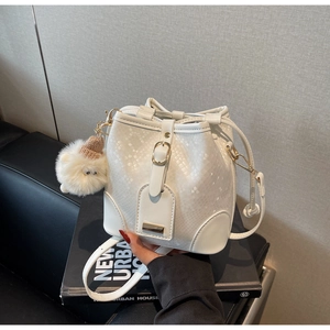Detail of white bucket bag featuring snake skin texture, gold clasp and plush ball charm