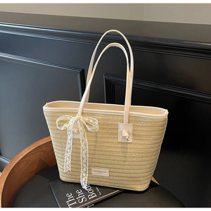 Détail d'un sac cabas en paille tressée avec bordure en cuir blanc et nœud en dentelle