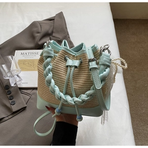 Detail of mint green woven handle and pearl charm on a straw bucket bag for summer