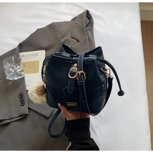 Close-up of dark blue snake embossed bucket bag with gold hardware and pompom charm