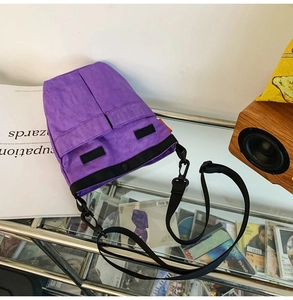 Dettaglio di borsa a tracolla in nylon viola con cinturino nero regolabile su vetro
