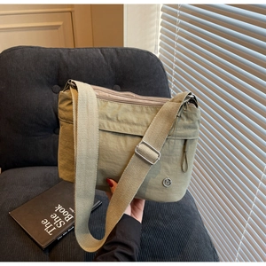 Detail of light green nylon tote with metal logo and strap on a corduroy sofa