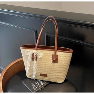 Détail d'un sac cabas en paille avec poignées en cuir marron et un nœud en dentelle blanche