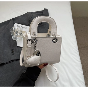 Detail of white litchi pattern handbag with heart pendant and metallic eyelets