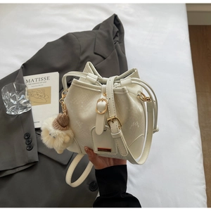 Detailed close-up of cream snakeskin bucket bag with plush charm and gold hardware