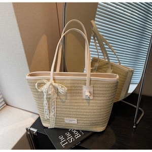 Détail d'un sac cabas en paille tressée avec anses en cuir blanc et nœud en dentelle