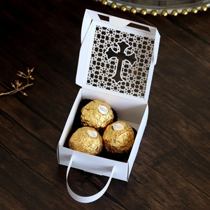 Macro view of white laser-cut hollow gift box with cross pattern and golden chocolates