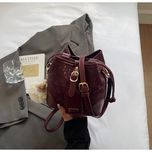 Detail of burgundy snakeskin bucket bag with adjustable strap and plush ball charm