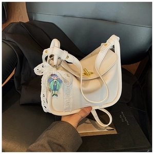 Detail der weißen Handtasche mit Lederstruktur, goldenem Drehverschluss und Spitzenschleife